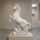 The Rearing Horse White Marble Outdoor Sculpture - 180cm by Giant Sculptures stands on a stone pedestal in a modern, minimalist gallery with neutral walls and soft natural light.