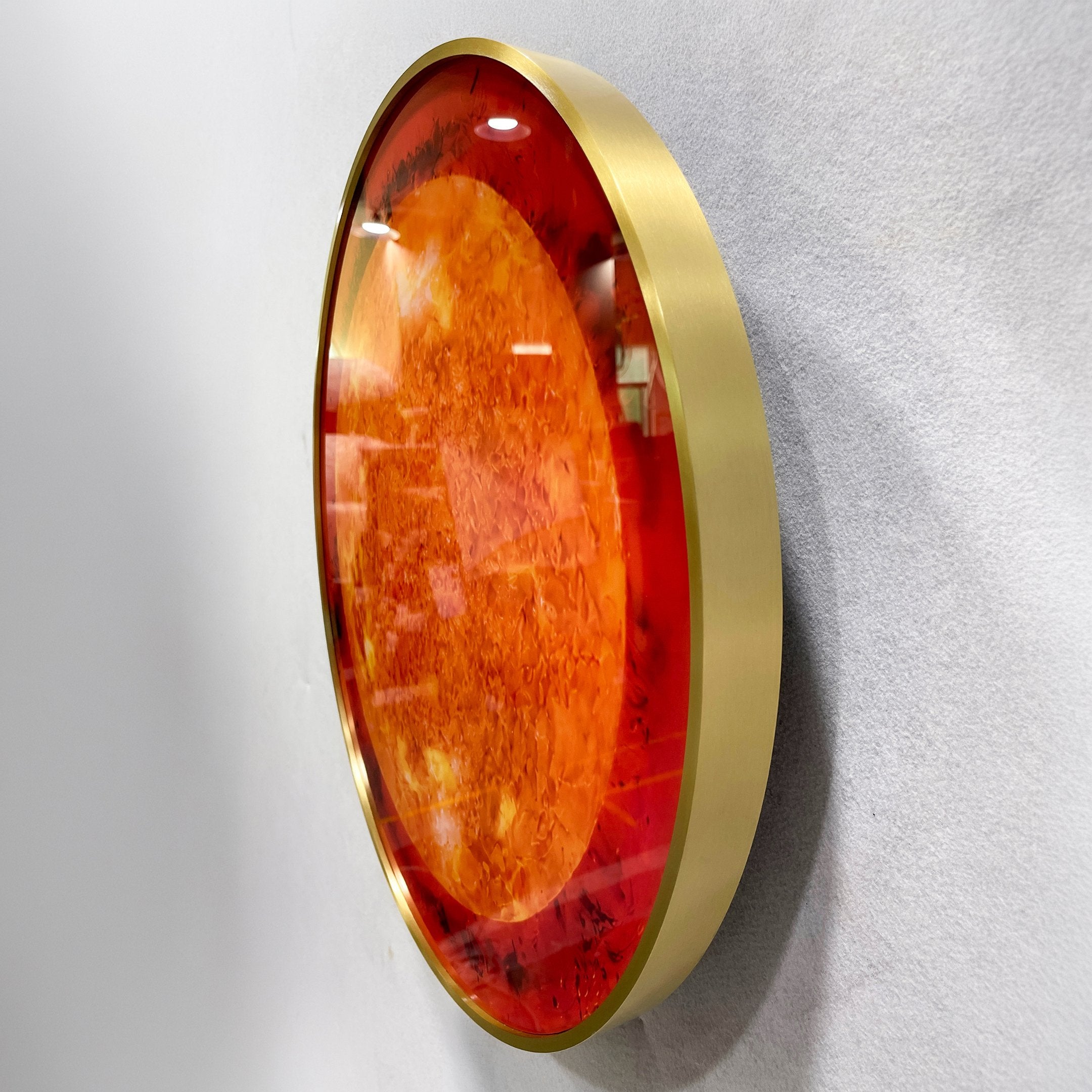 Side-angle view of the Galaxia Sun Crystal Porcelain LED Wall Art by Giant Sculptures, showing the domed amber and red sun motif within a brushed gold ring frame.