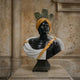 The Moorish Feather Turban Marble Bust Sculpture (85cm) by Giant Sculptures features a man with dark stone skin, a yellow feather turban, white and gold draped garment, and three green feather forms—striking decor for any stone wall.