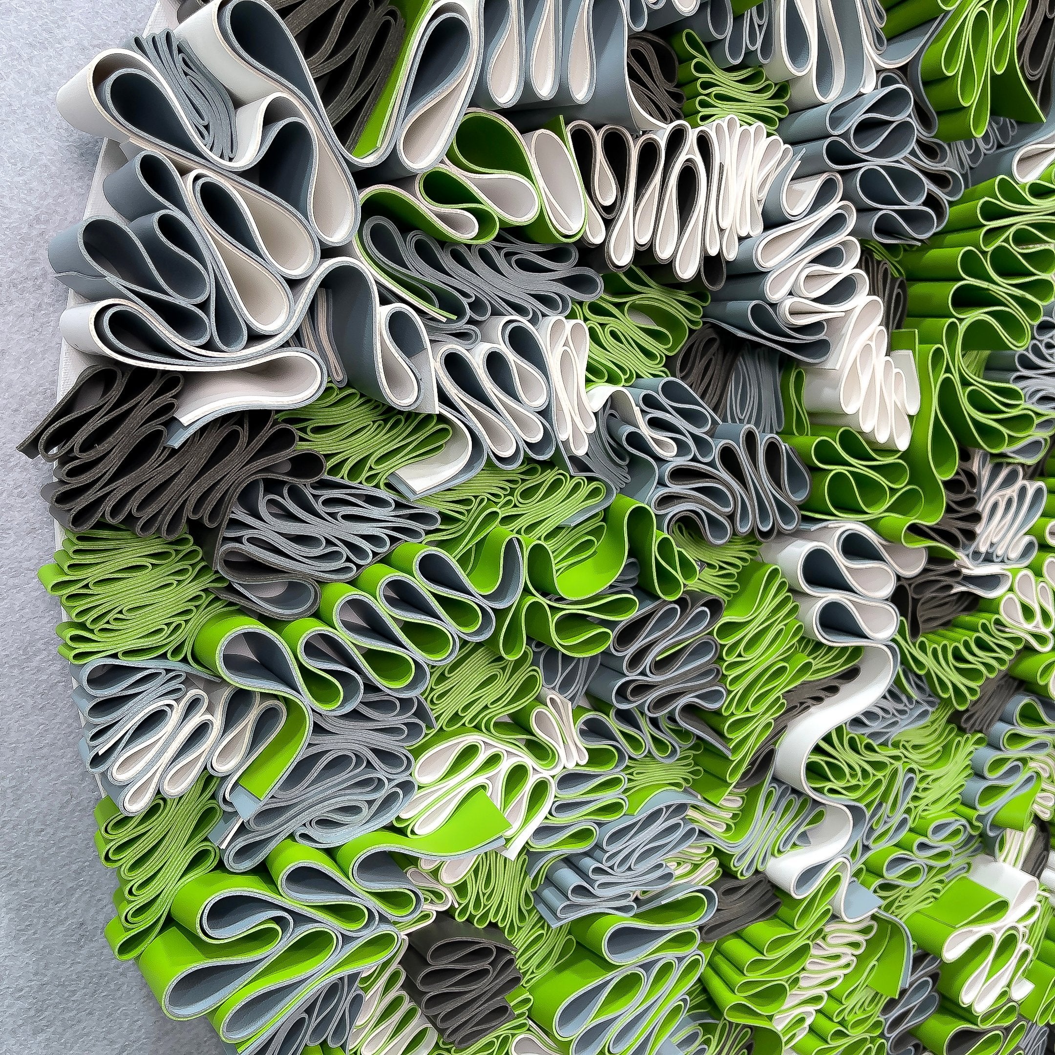 Close-up of the Giant Sculptures Rivora Green Ribbon Leather Circular 3D Wall Art, showing densely packed wavy leather ribbons in green, white, and grey tones.