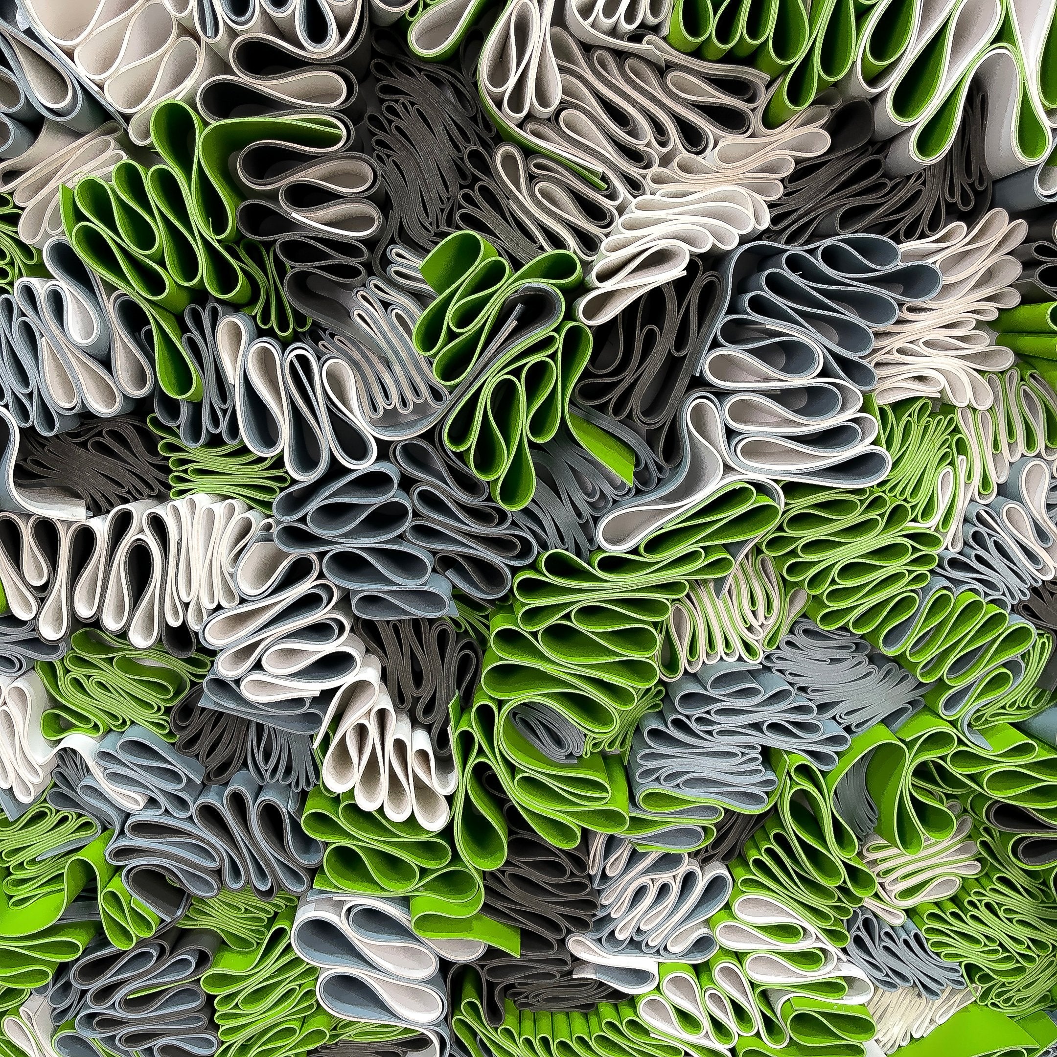 Close-up of the Giant Sculptures Rivora Green Ribbon Leather Circular 3D Wall Art, showing densely packed wavy leather ribbons in green, white, and grey tones.