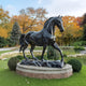 The Majestic Horse Black Marble Outdoor Sculpture (220cm) by Giant Sculptures stands proudly on a stone base in a landscaped park. Vibrant orange and gold autumn foliage, lush lawns, and manicured bushes in the background enhance its allure.