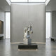 The Elegant Horse Head White Marble Outdoor Sculpture - 120cm by Giant Sculptures stands on a pedestal in a modern room with gray walls, polished flooring, and large skylights.