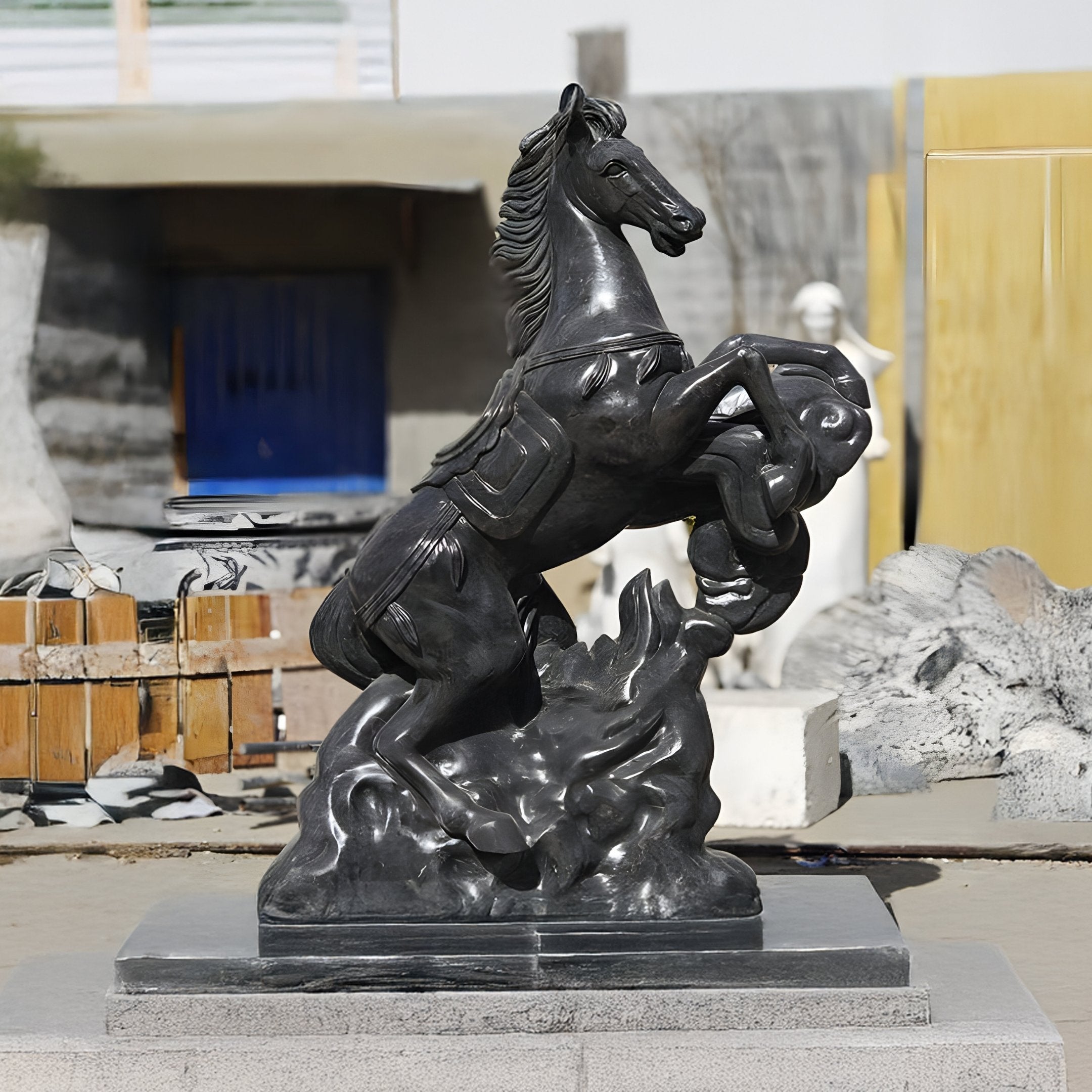 The Rearing Horse Black Marble Outdoor Sculpture - 200cm by Giant Sculptures stands majestically on a rectangular base, featuring a detailed mane and saddle. This striking piece is set against a blurred backdrop of construction materials and partial structures.