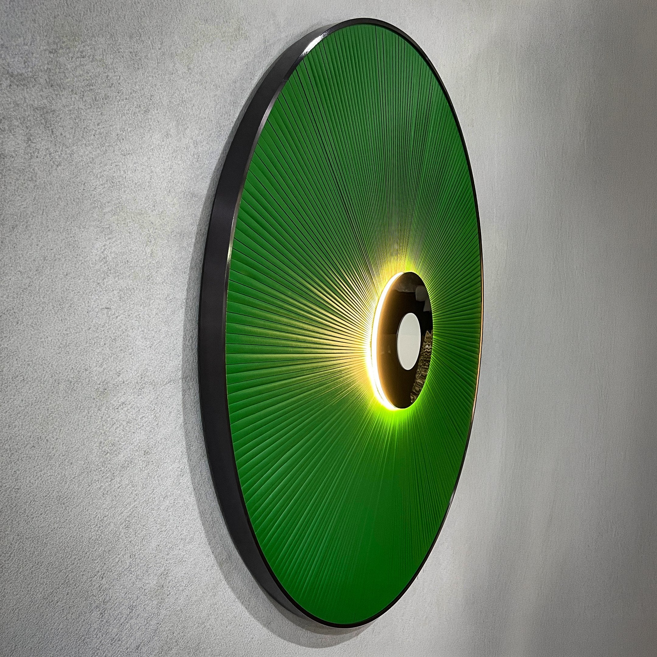 Side-angle view of the Vanguard Jade Surge Leather 3D LED Wall Art, showing jade-green leather rays radiating from a black central disc with glowing LED backlight on a grey wall.