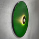 Side-angle view of the Vanguard Jade Surge Leather 3D LED Wall Art, showing jade-green leather rays radiating from a black central disc with glowing LED backlight on a grey wall.