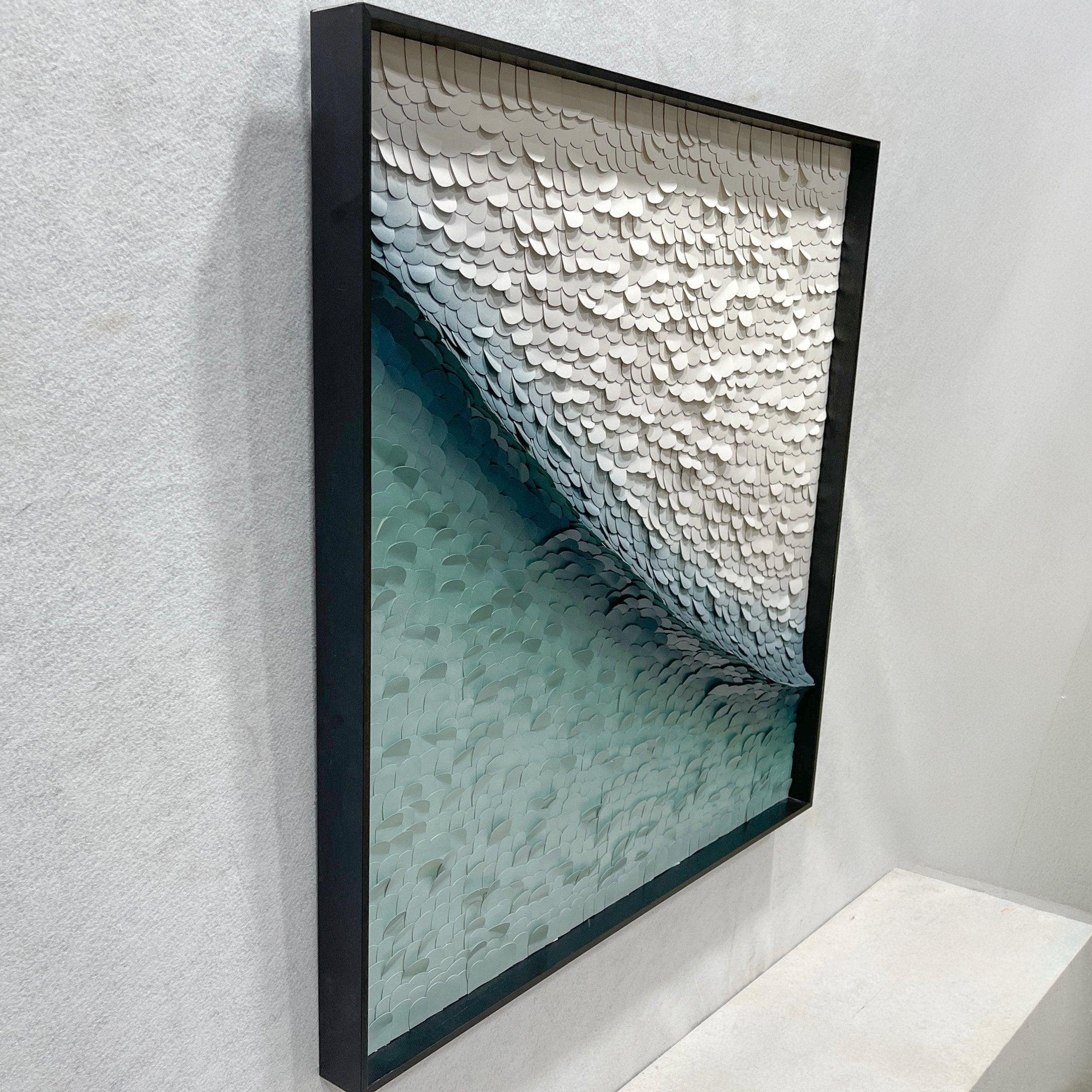 Side angle view of the Seravelle Mist Blue Gradient Layered 3D Paper Wall Art in a black shadow box frame, showing the textured wave of white and teal paper forms.