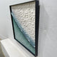 Seravelle Mist Blue Gradient Layered 3D Paper Wall Art shown at an angled side view in a black frame, revealing the depth of overlapping white-to-teal paper scales.