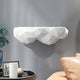 The White Geometric Cloud 3D Wall Shelf by Giant Sculptures, a functional décor piece, is mounted on a gray wall. To the left, a plant and decorative items adorn a black table; to the right, part of a beige leather sofa is visible.