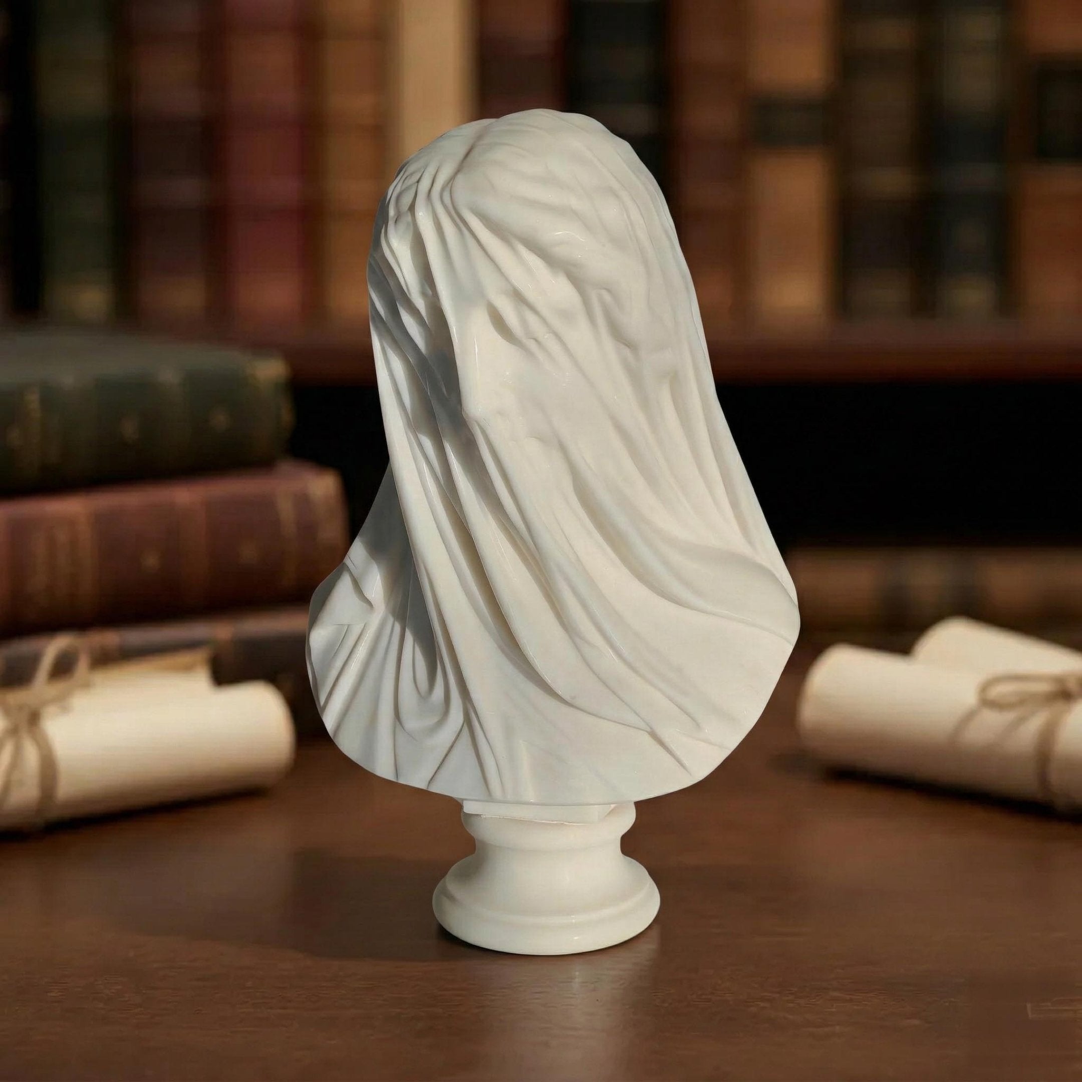 The Veiled Lady Marble Bust Sculpture - 55cm by Giant Sculptures is hand-carved from white marble and displayed on a wooden surface, with rolled scrolls and antique books elegantly arranged in the background.
