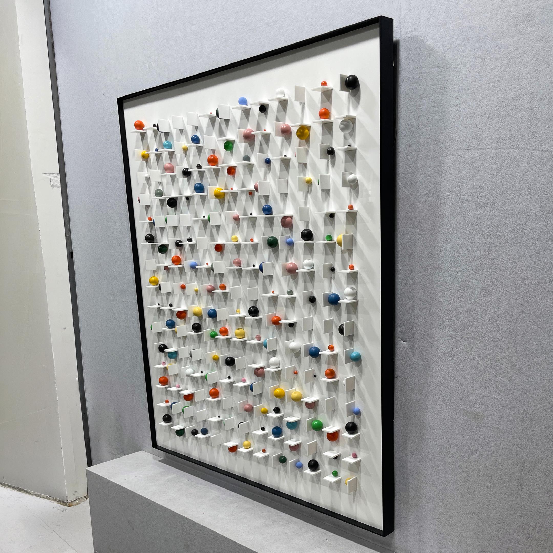 Aeris Multi-Coloured Wooden Sphere 3D Wall Art by Giant Sculptures shown at an angle, with colourful pegged spheres on a white grid in a black frame.