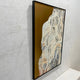 Aurista Botanical Flow Abstract Cotton Spray Wall Art viewed at an angle, showing raised beige and black leaf forms on a metallic gold ground in a black frame.