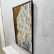Aurista Botanical Flow Abstract Cotton Spray Wall Art shown at an angle, with raised beige, white, black, and blue leaf forms on a gold ground in a black frame.