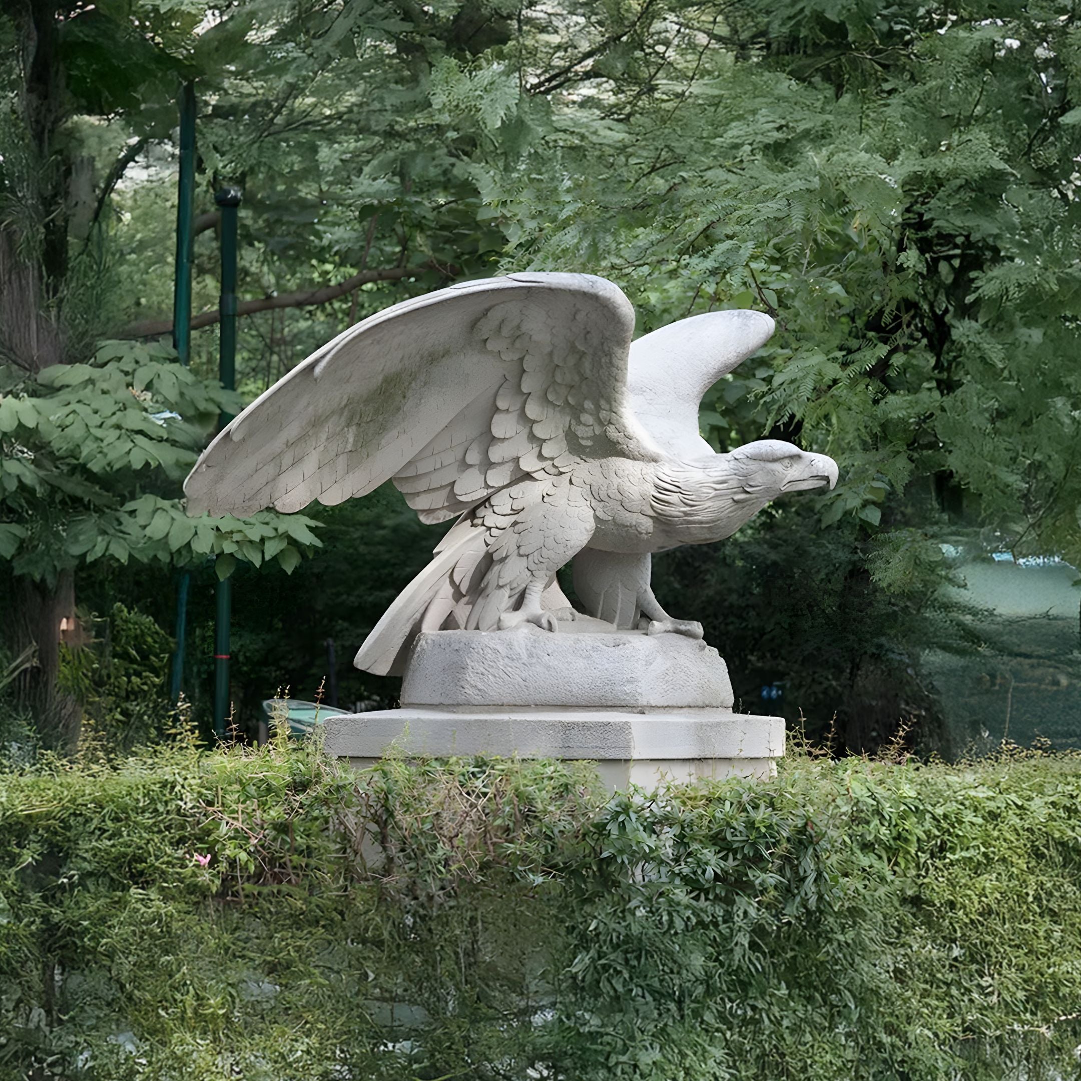 The Steadfast Gaze Eagle Marble Outdoor Sculpture - 120cm by Giant Sculptures majestically perches with wings partially extended on a rectangular pedestal, surrounded by lush green foliage.