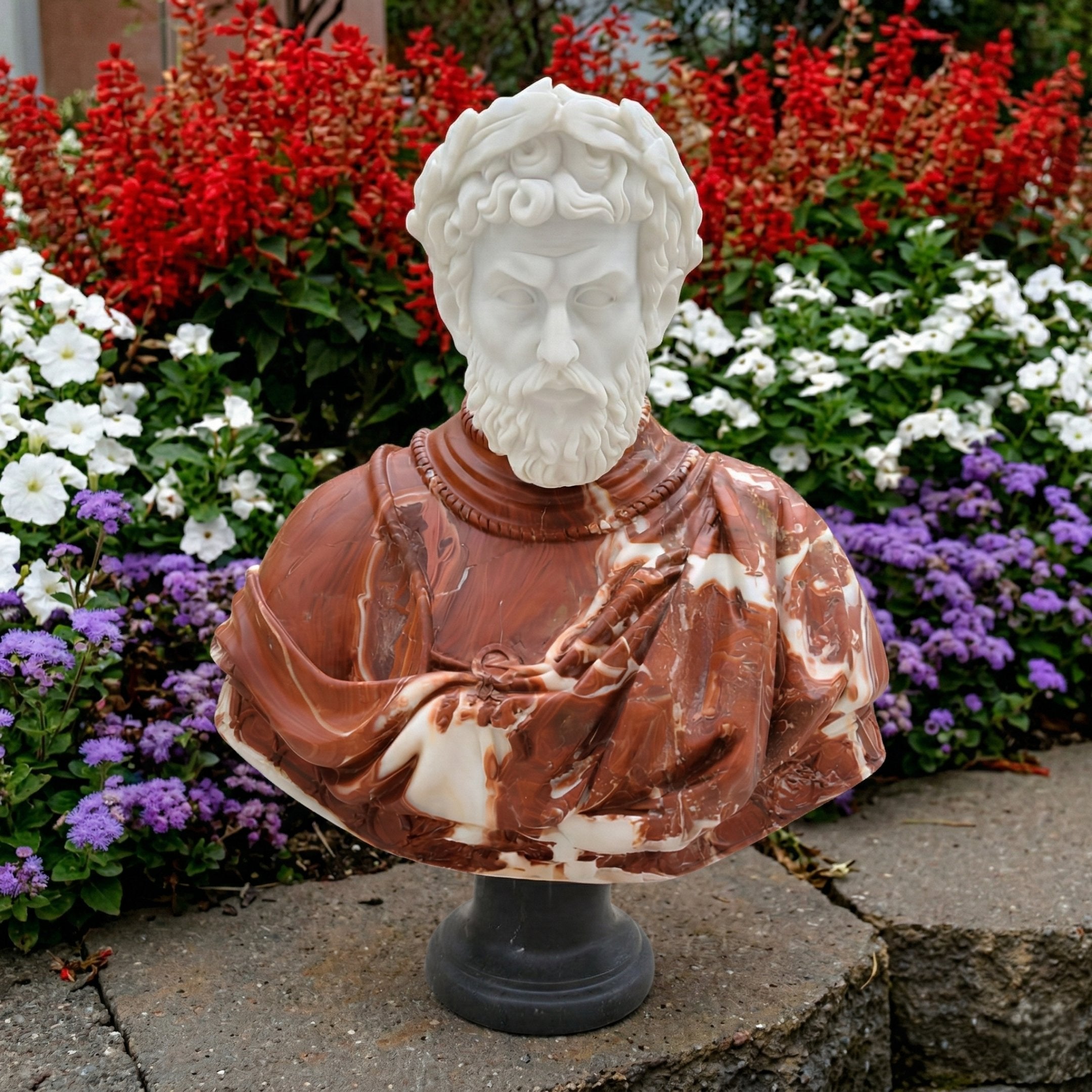 The Roman Emperor Marble Bust Sculpture - 75cm by Giant Sculptures depicts a bearded man with curly hair, outdoors among vibrant red, white, and purple flowers. His robe is carved from brown and white marble.