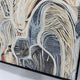 Close-up angled view of the Aurista Botanical Flow Abstract Cotton Spray Wall Art showing raised beige, white, and blue leaf forms over a metallic gold ground.