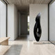 Abstract Flame Marble Sculpture by Giant Sculptures in black marble on a stone plinth, displayed in a minimalist concrete hallway beside a pale wood bench.