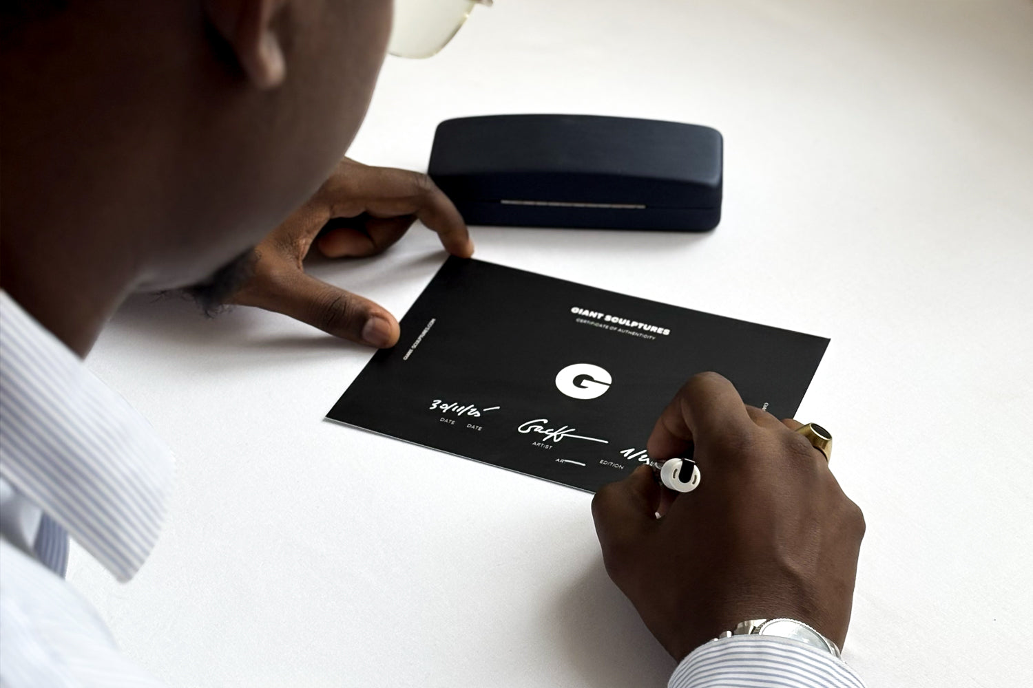 Artist Andre Gacko signing giant sculptures certificate with a pen on a white surface
