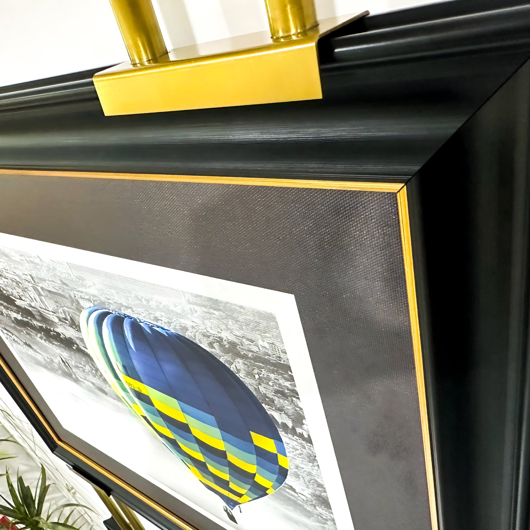 The Imperia Vibrant Balloon Journey Dual Frame Metal Wall Art by Giant Sculptures showcases a colorful hot air balloon in blue, yellow, and green against a grayscale cityscape, featuring a black frame with gold trim and an elegant gold metal accent on top.