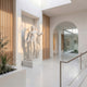 Eros Genie Of Borghese Angel Marble Outdoor Sculpture by Giant Sculptures, 180cm white marble figure with outstretched wings in contrapposto stance, displayed in a bright modern hallway with arched doorway and wooden slat accents.