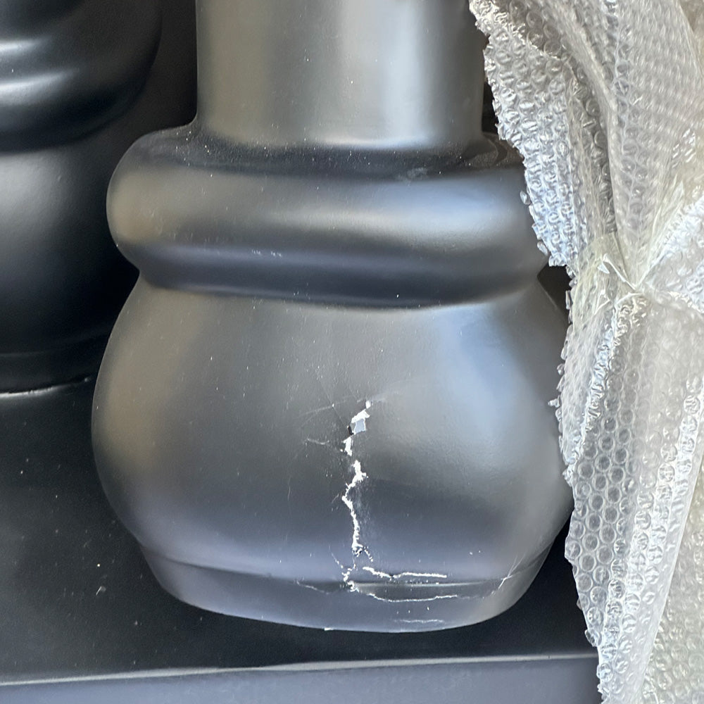 A close-up of the Giant Sculptures Midnight Black Iconify Family Sculpture - 200cm (Ex Display), a modern resin piece with a rounded shape, visible crack, and surface scratches. Bubble wrap partially covers its right side.