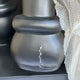 A close-up of the Giant Sculptures Midnight Black Iconify Family Sculpture - 200cm (Ex Display), a modern resin piece with a rounded shape, visible crack, and surface scratches. Bubble wrap partially covers its right side.