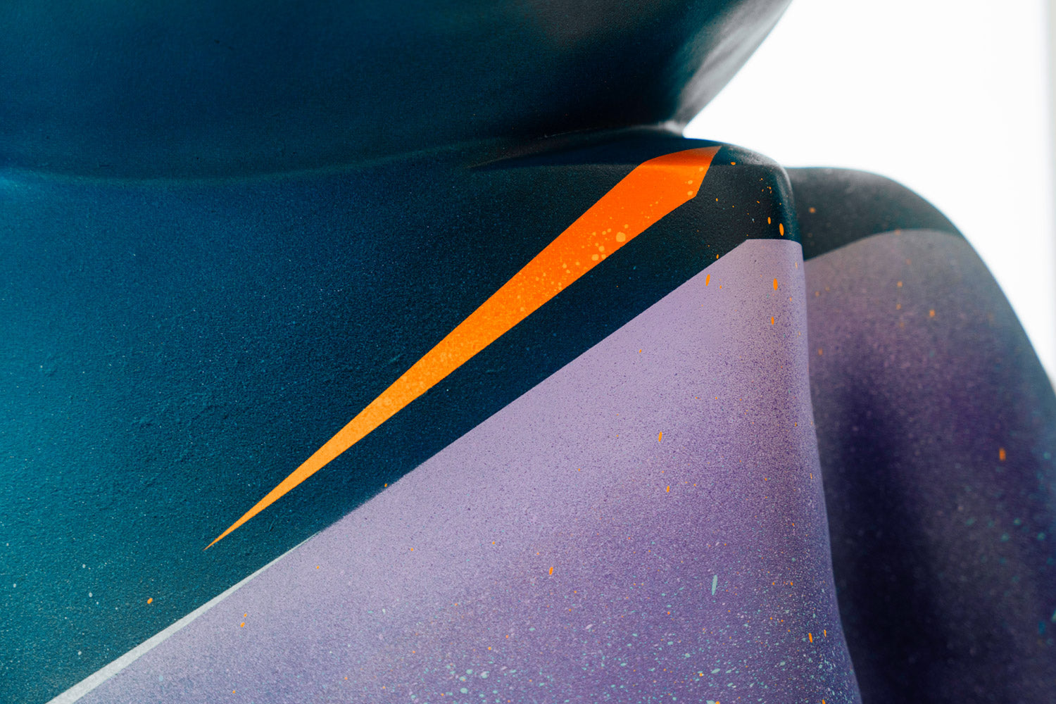 Close-up of a modern abstract sculpture featuring smooth, overlapping surfaces in shades of blue and purple. An orange diagonal line streaks across the design, adding a dynamic contrast to the composition.