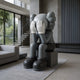 The large 163cm Slate Grey Iconify Melancholy Sitting Sculpture by Giant Sculptures features a seated cartoon-like figure with gloved hands covering its face. Its glossy gray finish and exaggerated features add contemporary charm to modern, minimalist interiors with large windows and a neutral palette.