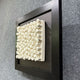 The Harmonia 3D Spiral Wall Sculpture by Giant Sculptures features numerous upright white ceramic spirals on a rectangular base, framed in black—creating a striking textured effect ideal for modern spaces.