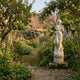 Giant Sculptures' 210cm Female Figure with Pedestal Marble Sculpture on a stone path in a cottage garden with foxgloves, delphiniums, and roses.