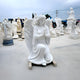 The Kneeling Serenity Angel Marble Outdoor Sculpture from Giant Sculptures, standing at 150cm, depicts a kneeling angel with clasped hands in prayer. Complete with detailed wings and a serene expression, it is set among other marble statues on a smooth, light-toned surface.