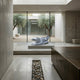 A modern minimalist room with concrete walls, large windows, and a rocky feature. An inflatable alligator pool float rests on a platform, while olive trees and the Crocodile II White Marble Outdoor Sculpture by Giant Sculptures are visible outside.
