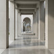 The Ornate Camel White Marble Outdoor Sculpture (160cm) by Giant Sculptures stands on a pedestal at the corridor's end, framed by tall stone columns and reflective flooring in a sleek modern architectural space.