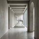 The Classic Caravan Camel Marble Outdoor Sculpture - 160cm by Giant Sculptures is showcased in a minimalist concrete hallway with large windows and high ceilings, evoking the timeless elegance of classic caravan decor.