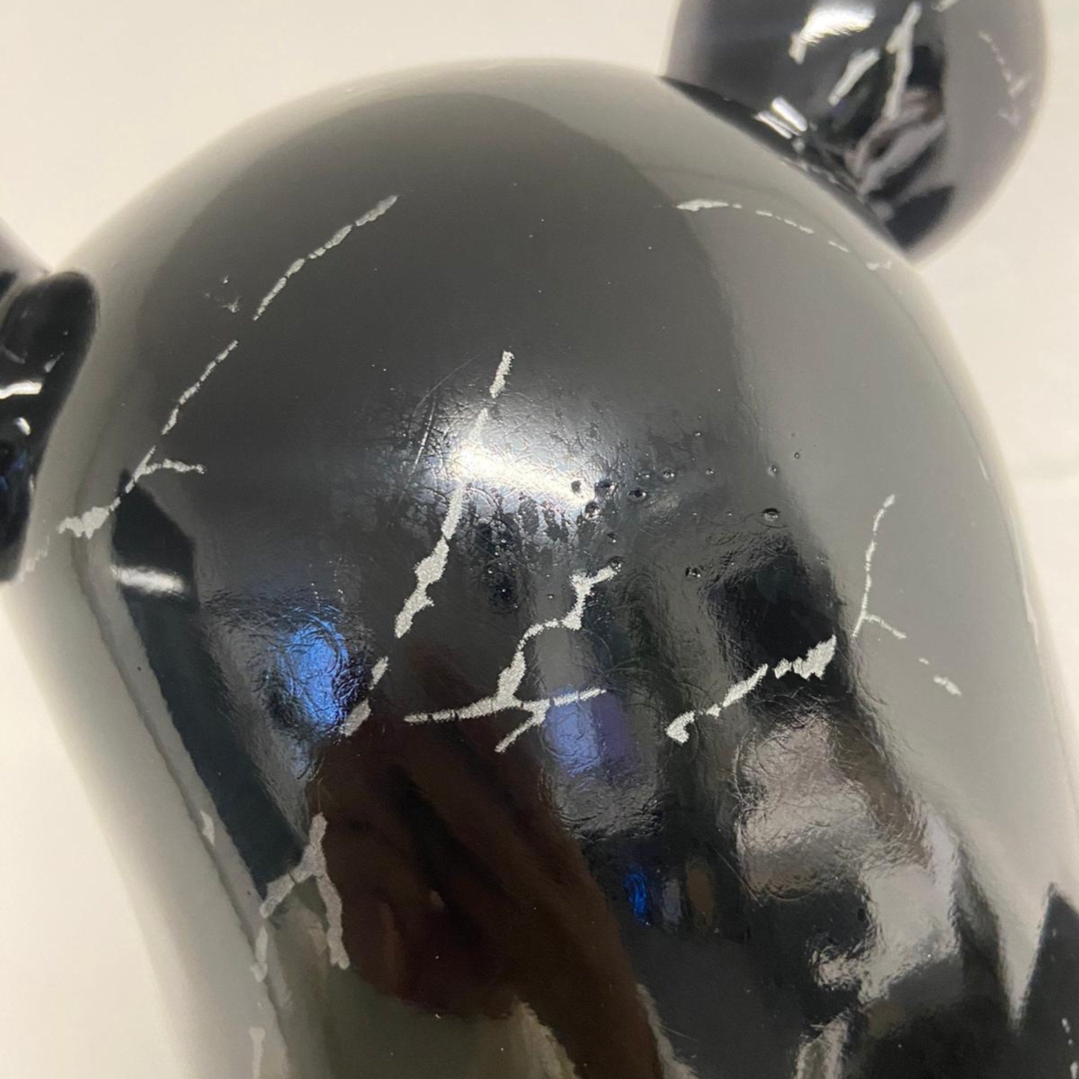 Close-up of the 50cm Black Stone Bear Sculpture by Giant Sculptures, ex-display piece, with visible white scratches and scuffs. Shiny surface, blue hues, and faint reflection enhance its modern interior decor appeal.