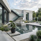 A modern courtyard features the Steadfast Gaze Eagle Marble Outdoor Sculpture (120cm) by Giant Sculptures as a centerpiece in a rectangular reflecting pool, surrounded by concrete, glass railings, and minimalistic green landscaping.