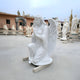 In a peaceful garden, the Serene Kneeling Angel Marble Outdoor Sculpture by Giant Sculptures stands at 130cm. Crafted from white marble, this angel kneels with clasped hands and wide-spread wings, surrounded by other statues. Its a tribute to peace and reflection against a clear sky.