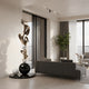 A modern living room features a gray sofa, large windows with sheer curtains, and the Balance Bronze Abstract Steel Sculpture (180cm) by Giant Sculptures as the centerpiece. Minimalist decor, neutral tones, and a potted plant complete the contemporary space.