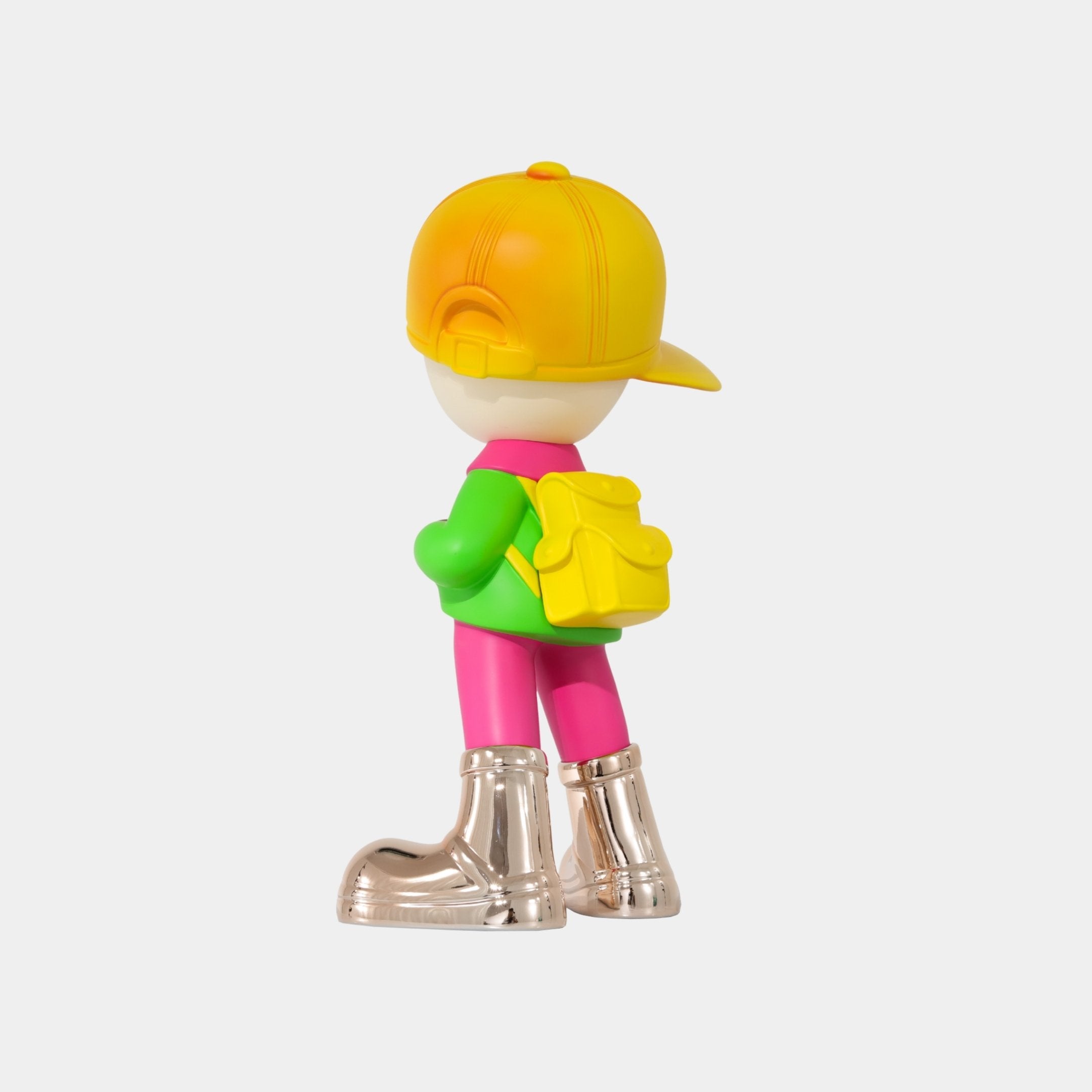 The Giant Sculptures Electroplated Boots & Fist Sunset Brimble Figure (52cm) features a boy facing away in a yellow cap, green shirt, pink pants, yellow backpack, and shiny electroplated boots against a plain white background.