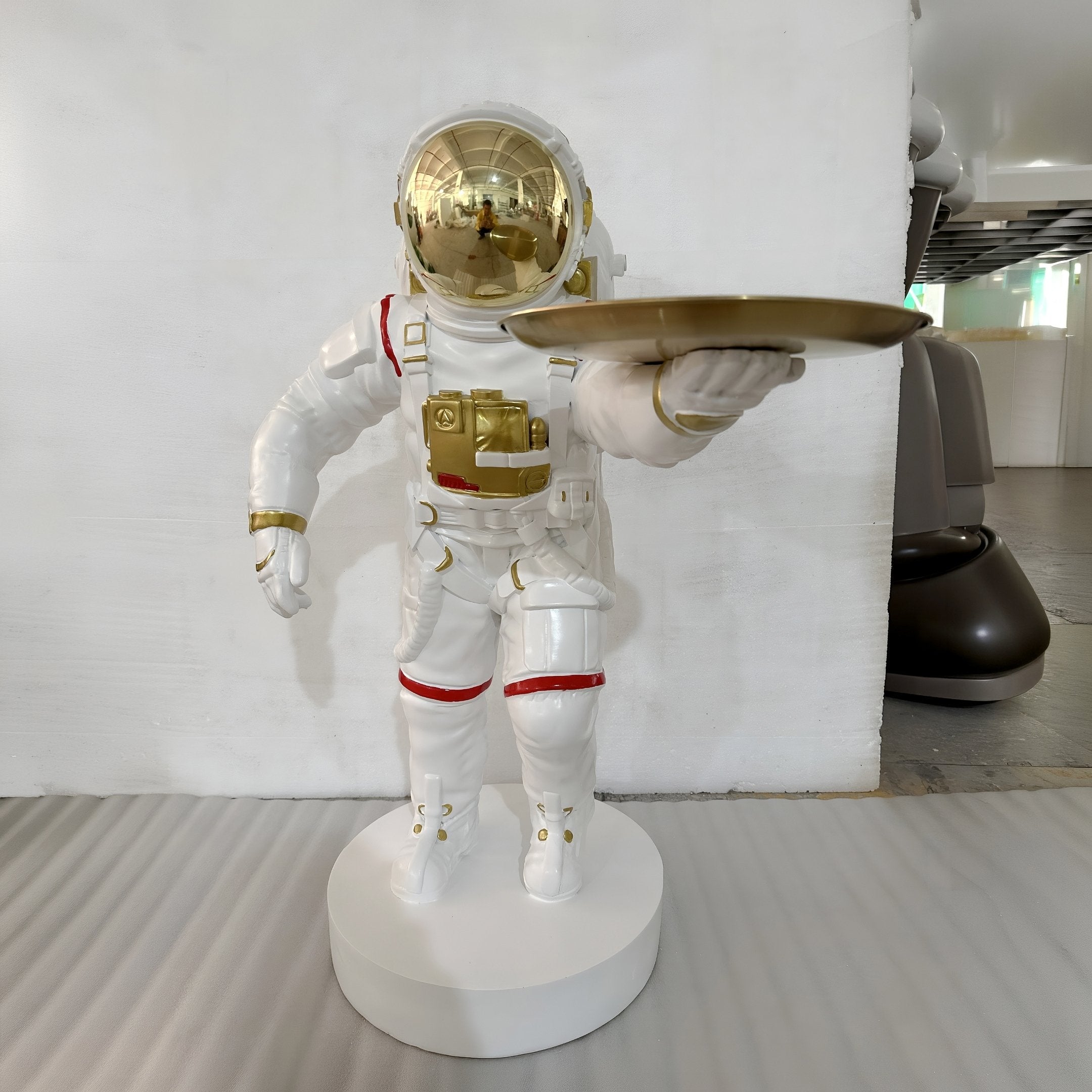 The Giant Sculptures White Space Astronaut Explorer Serve Sculpture (85cm) features a white astronaut with gold accents holding a gold tray on a round base—ideal as standout space-themed decor against a white wall.