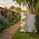 Monument Tombstone Angel Marble Outdoor Sculpture by Giant Sculptures, 120cm white marble angel leaning against a curved headstone, displayed in a walled garden with roses and delphiniums.