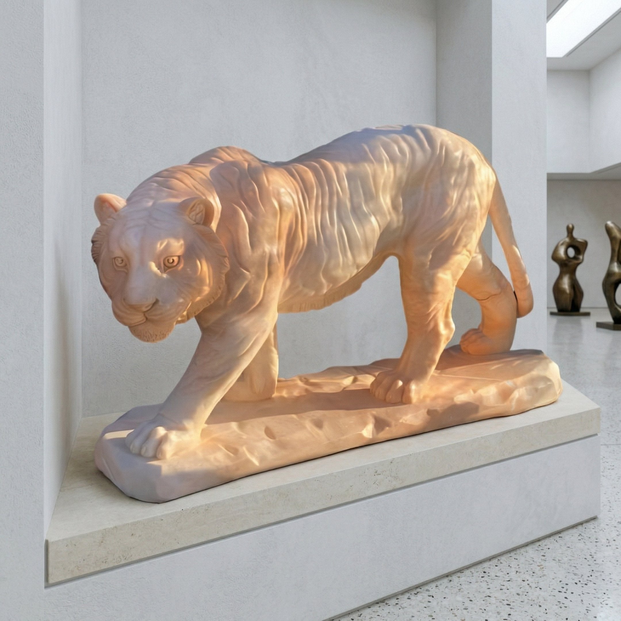 The Striding Tiger Yellow Marble Outdoor Sculpture (60cm) by Giant Sculptures stands on a stone pedestal in a modern, white-walled gallery, with abstract human-shaped statues visible in the background.