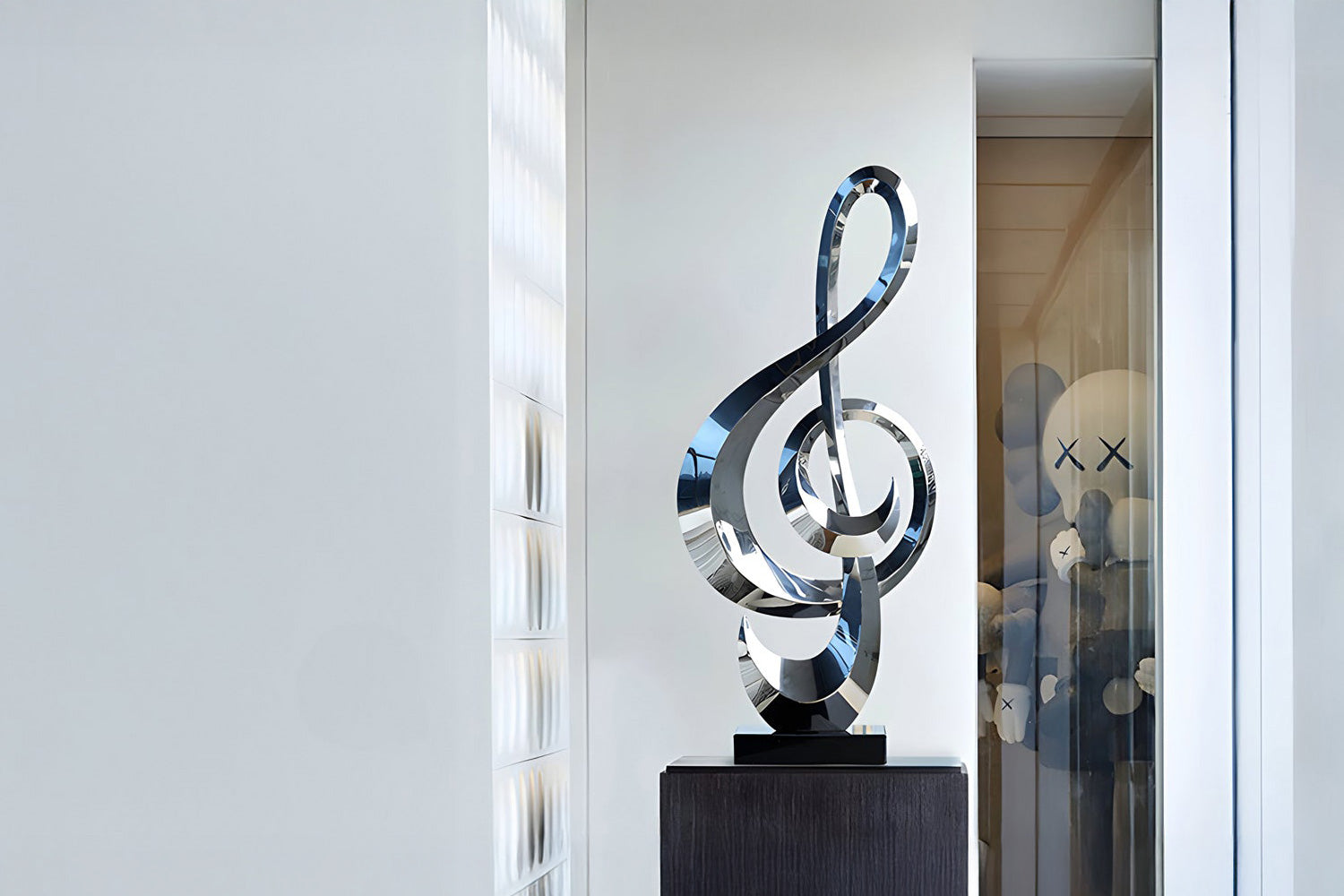 A sleek, modern sculpture resembling a treble clef stands on a pedestal in a well-lit room. In the background, blurred abstract figures with X eyes can be seen through a glass partition.