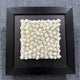 The Harmonia 3D Spiral Wall Sculpture With Black Frame by Giant Sculptures features small, white, rolled paper-like shapes arranged in a grid on black—an elegant square piece ideal for contemporary spaces.