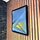 The Skull&Stone II Abstract Canvas Wall Art by Giant Sculptures, featuring sharp blue and yellow geometric shapes, is displayed framed on a wooden slat wall beside a black brick section.