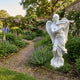 Angel Playing Violin Angel Marble Outdoor Sculpture in white marble, 180cm tall, depicting a winged angel mid-performance in a lush walled English garden with climbing roses and lavender.