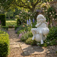 Cherub V4 Angel Marble Outdoor Sculpture by Giant Sculptures, 80cm white marble figure seated in a thoughtful pose amid a lush English garden with roses and delphiniums.