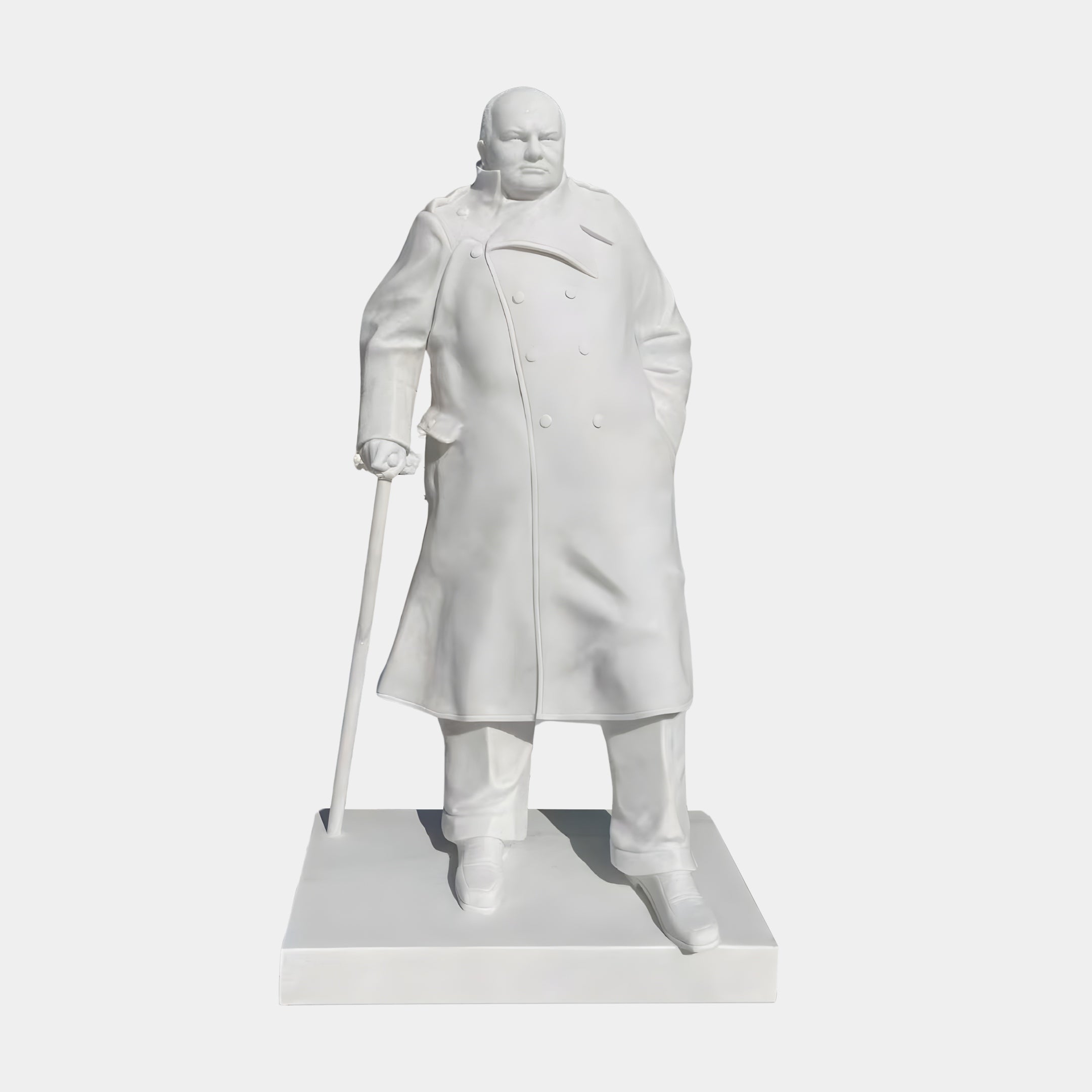 The Winston Churchill Marble Outdoor Sculpture - 195cm by Giant Sculptures depicts Churchill in a long coat on a rectangular base, holding a cane in his right hand with his left hand in his pocket, looking straight ahead.