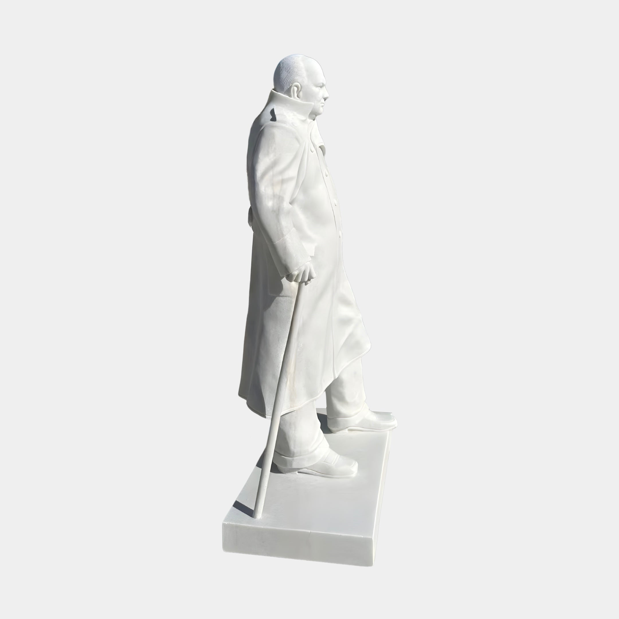 The Giant Sculptures Winston Churchill Marble Outdoor Sculpture (195cm) shows a man in a long coat on a rectangular base holding a cane and gazing forward. The background is plain, light gray.