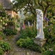 Giant Sculptures Venus de Milo 180cm white marble statue on a weathered stone plinth in a cottage garden with foxgloves, roses, and an apple tree.